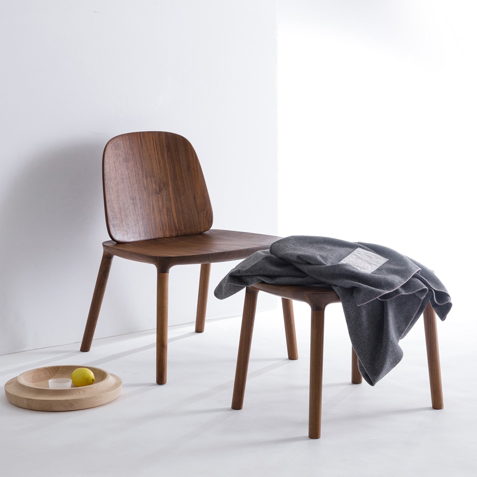 Kokoro Lounge Chair in walnut dark paired with Kokoro Ottoman, styled with a wool throw, emphasizing versatility and elegance. Raw WAAN bowl on side