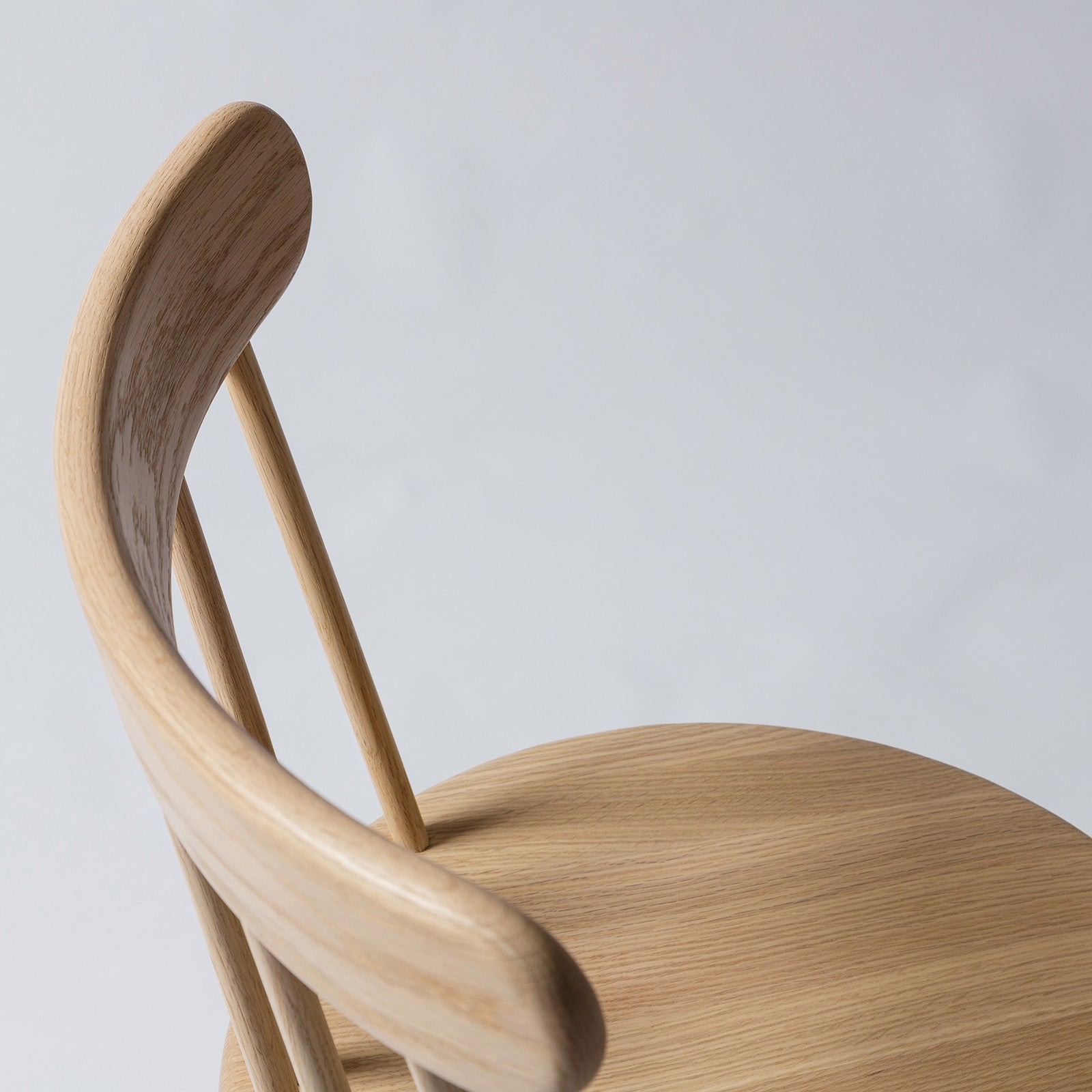 Close-up view of the Ai Chair in natural oak, showcasing the curved backrest and smooth wood grain for ergonomic comfort.
