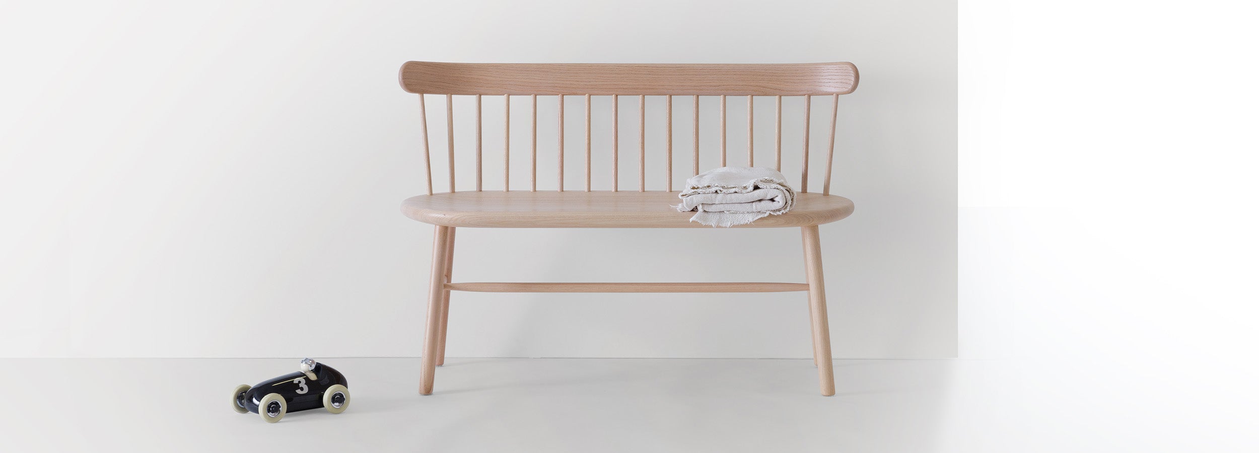 Ai Settee in natural oak finish, styled with a folded linen throw, showcasing its elegant spindled backrest and minimalist design.