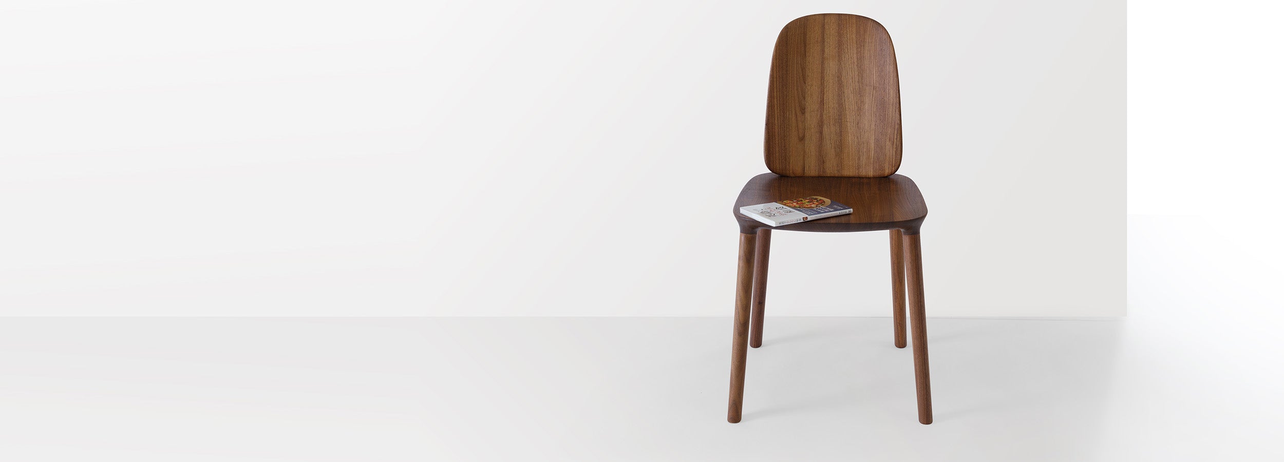 Kokoro Chair in walnut dark, placed in a minimalist setting, showcasing its soft lines and sculptural silhouette.