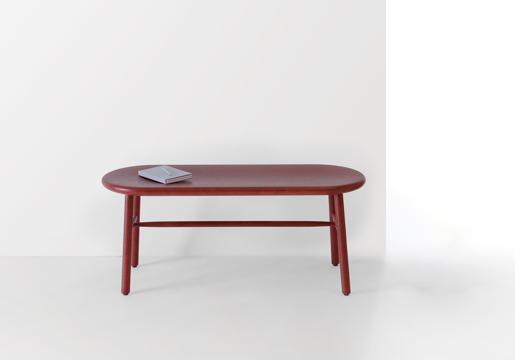 Ai Bench in deep red finish, showcasing its minimalist design and smooth craftsmanship in a bright, modern setting.