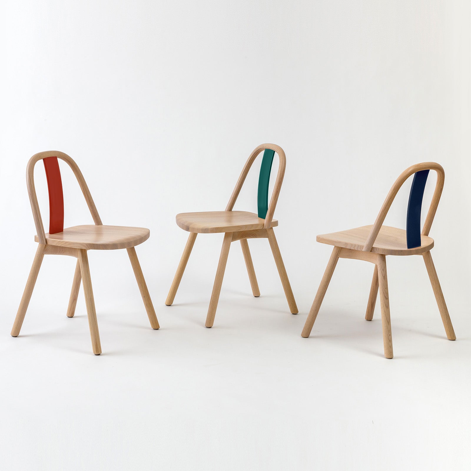 hree Chin-Chin chairs in oak with backrests in glossy red, emerald green, and navy blue finishes, showcasing the vibrant design options inspired by traditional Chinese craftsmanship.