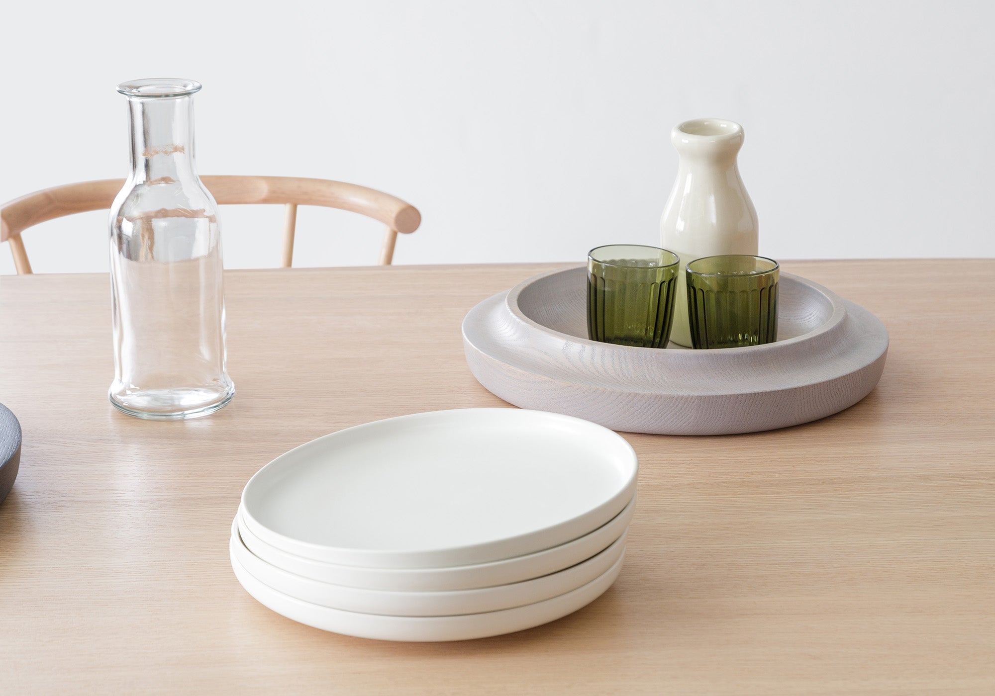 The Studio Table paired with the Studio Side Chair, styled with the Waan Bowl, a water carafe, stacked plates, and a glass, showcasing a clean and minimalist dining setup.