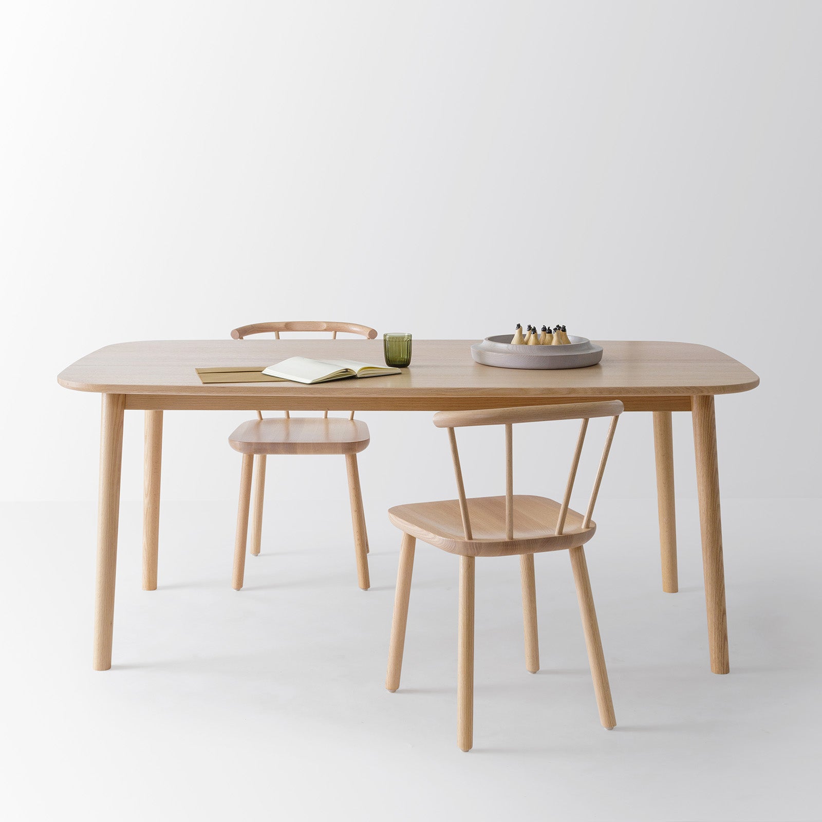 Studio Table paired with Studio Side Chairs, featuring a clean tabletop arrangement with books, a green mug, and a play set, in WAAN bowl, emphasizing a functional and elegant design.