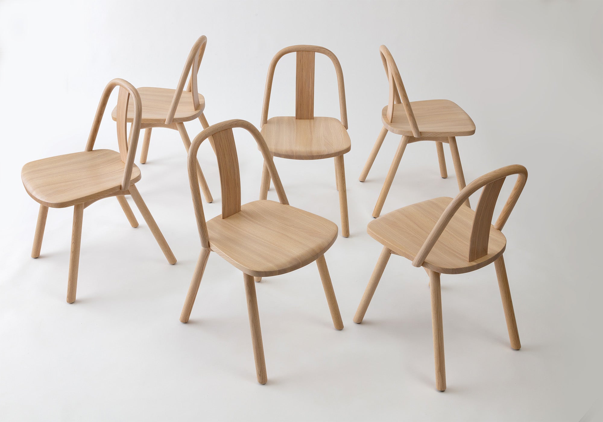A collection of Chin-Chin chairs crafted in natural oak, showcasing their minimalist curved design and versatile aesthetic for dining or gathering spaces.
