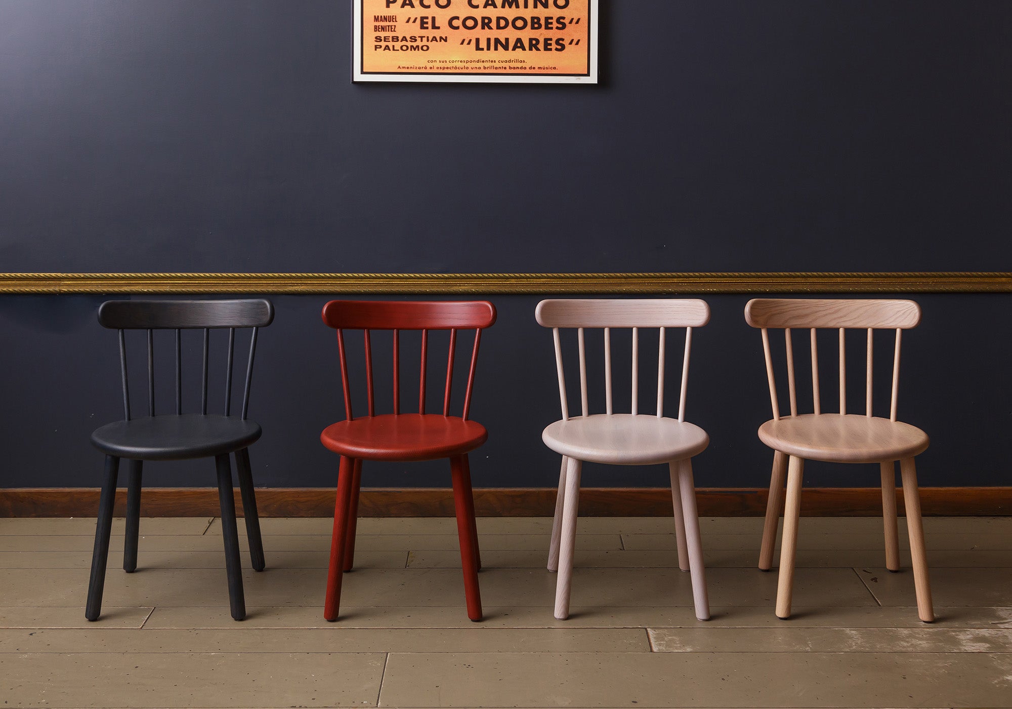 i Chairs in various finishes, including black, red, off-white grey, and natural oak, arranged against a dark navy wall to showcase their color options and classic spindled design.
