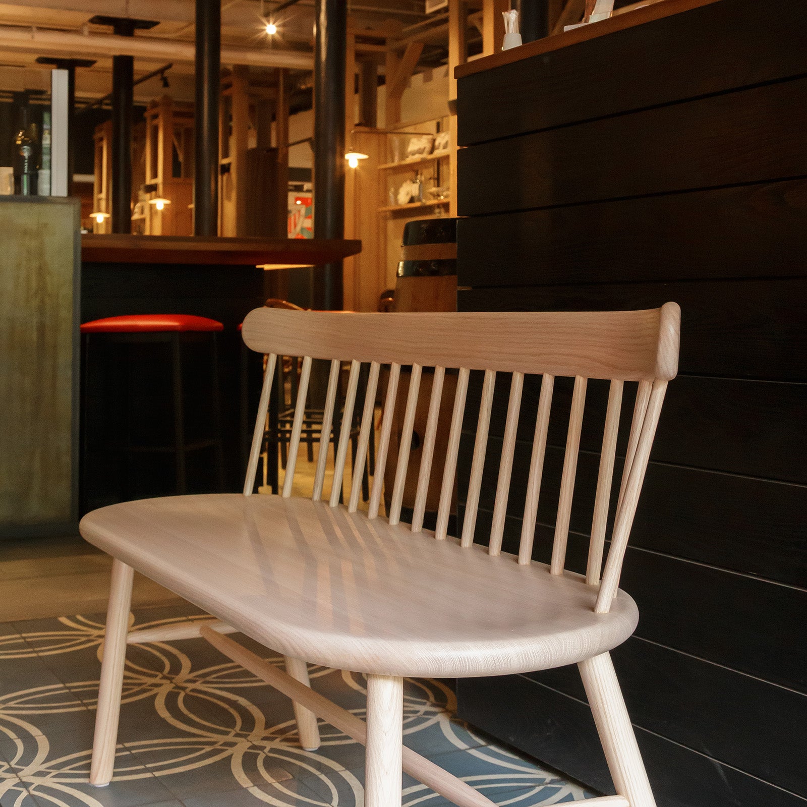 Ai Settee in natural oak, styled in a modern restaurant interior with warm lighting and sleek decor.
