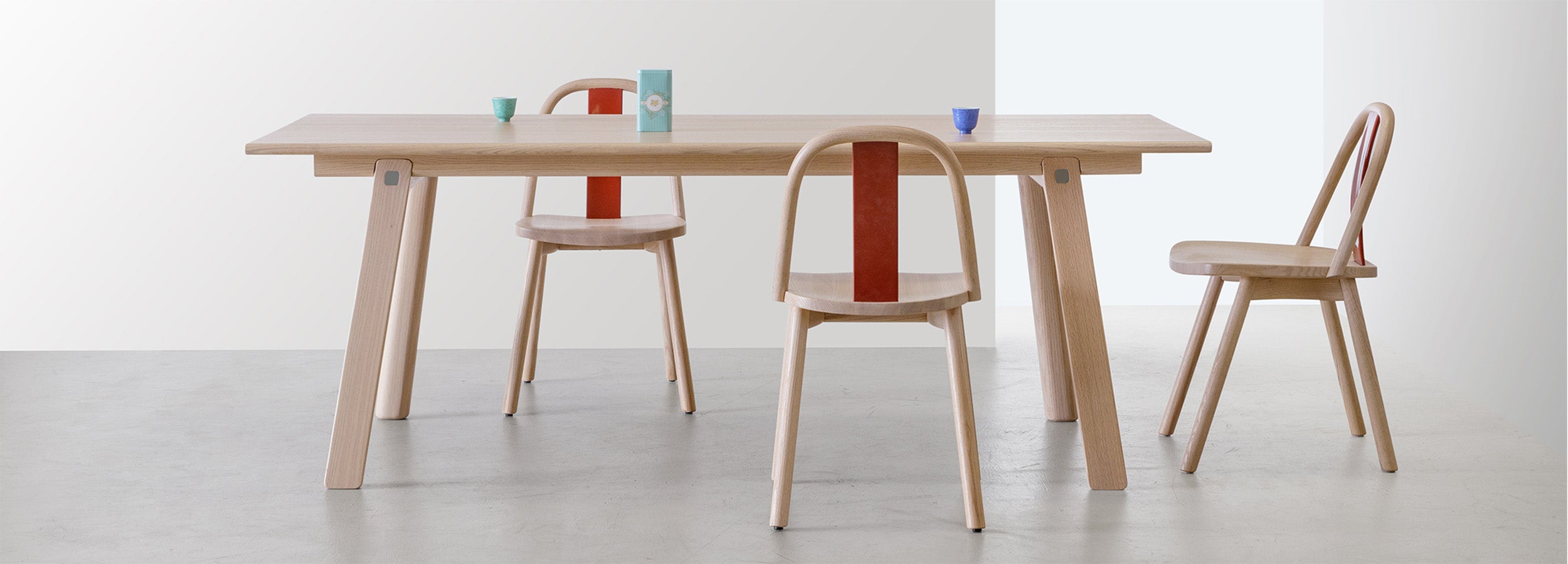 Chin-Chin chairs in natural oak with vibrant red lacquered backrest, set around a minimalist wooden dining table, inspired by Hong Kong’s street life and elegance.